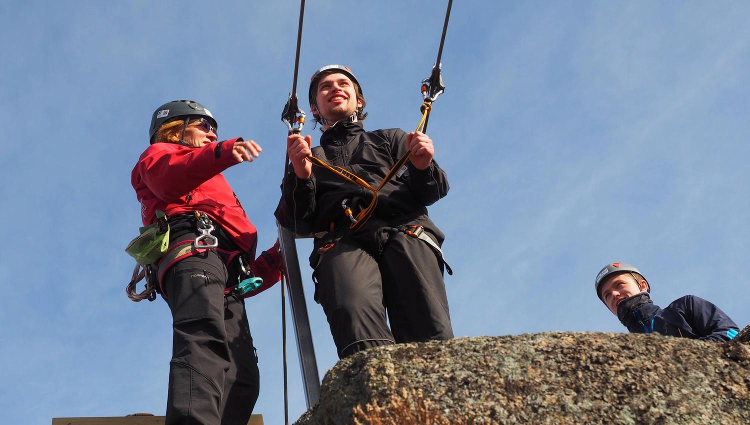Berit instruerer en ung mann på vei ut i zipline. Bak står nestemann og venter på tur.