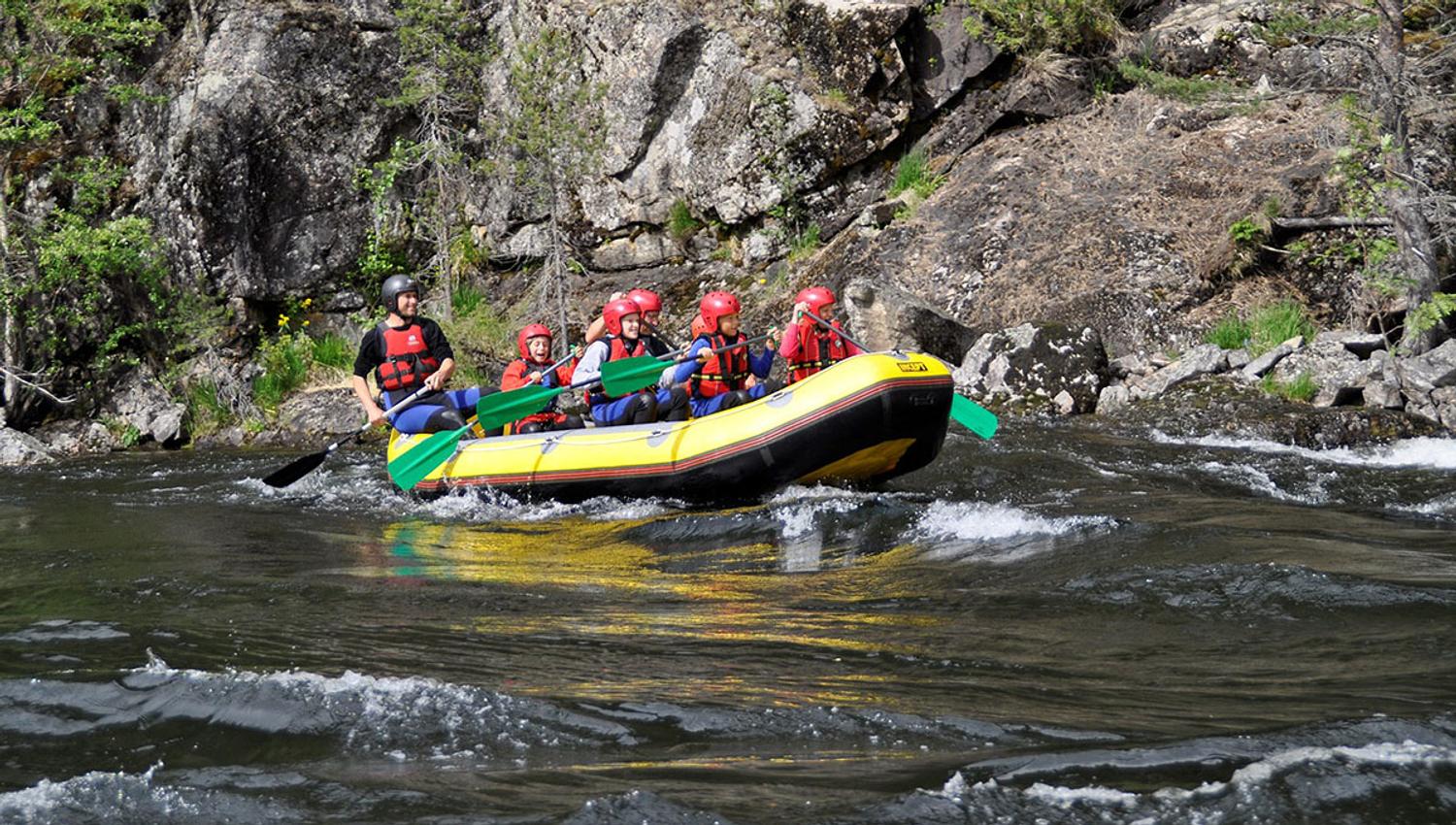 A yellow raft on a river passes a rock face
