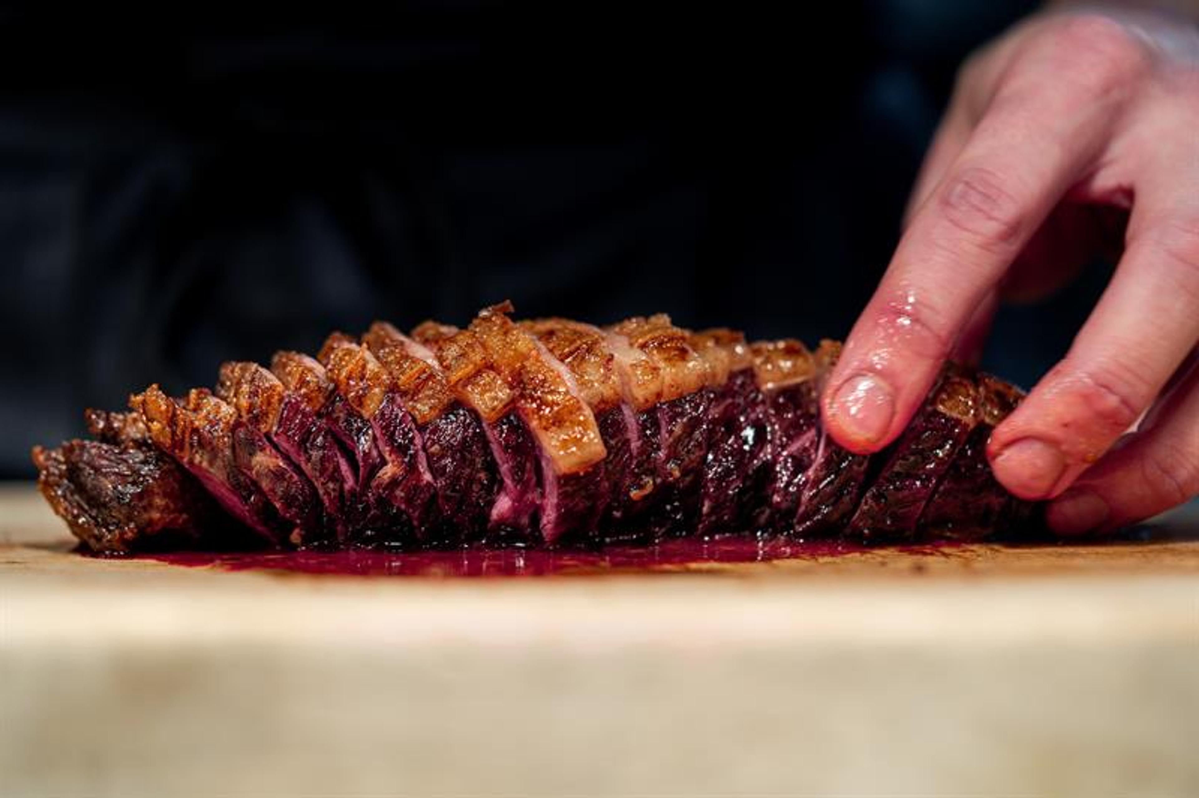 En hånd som holder et oppkuttet, grillet kjøttstykke