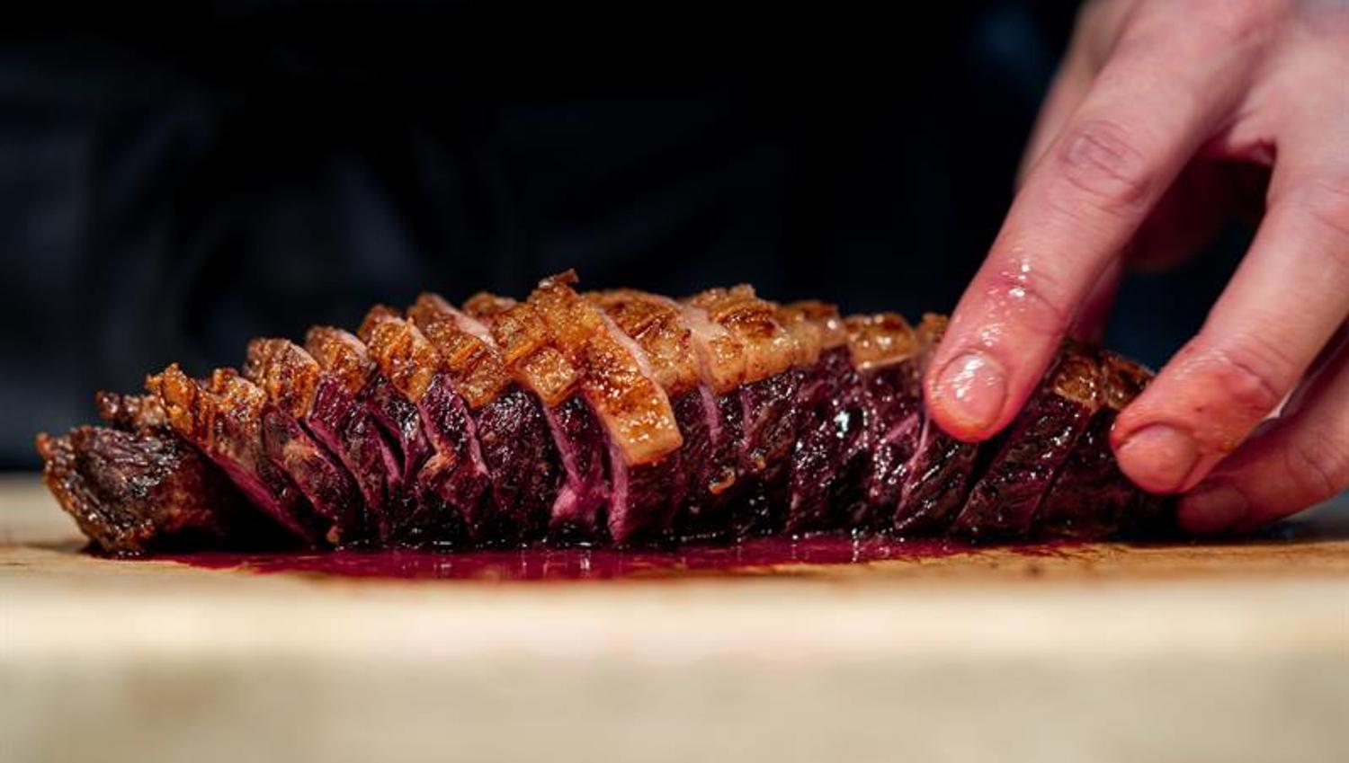 A hand holding a sliced piece of grilled meat