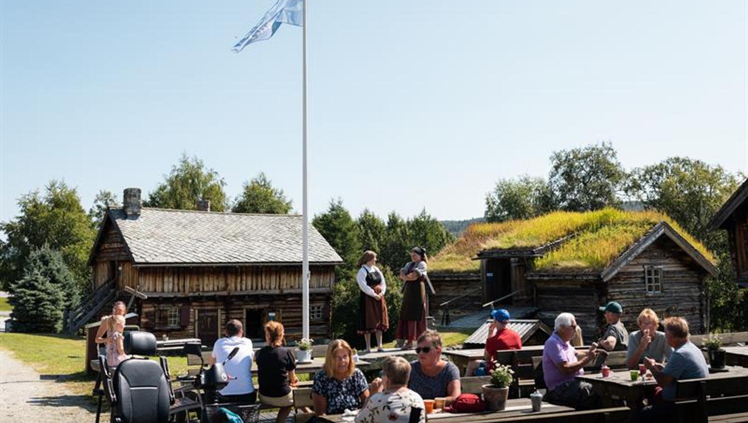 People are sitting in fornt of the serving hut at Geilojordet and watch theatre.