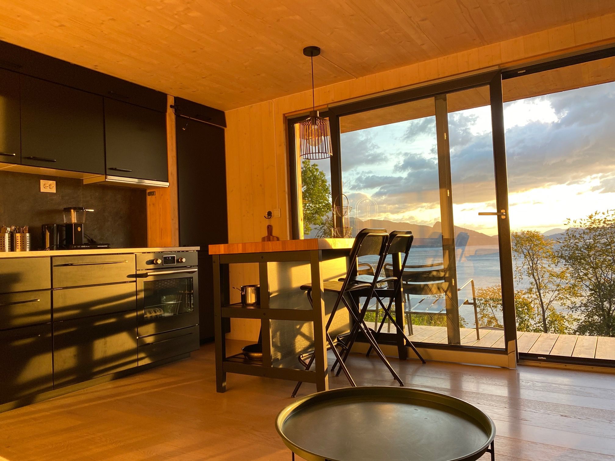 Kitchen and dining area in the cabin with sunset over the fjord in the background.