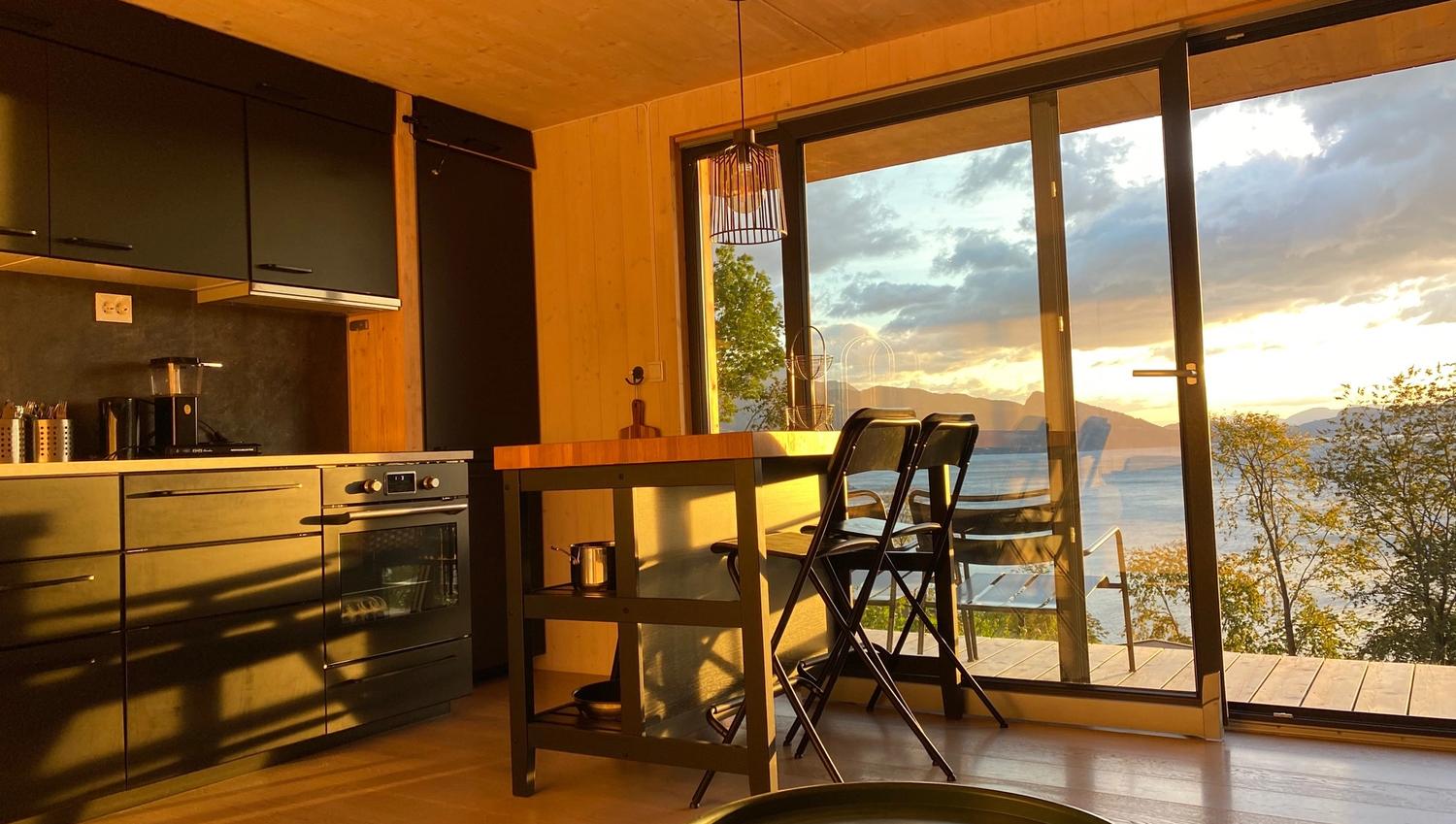 Kitchen and dining area in the cabin with sunset over the fjord in the background.