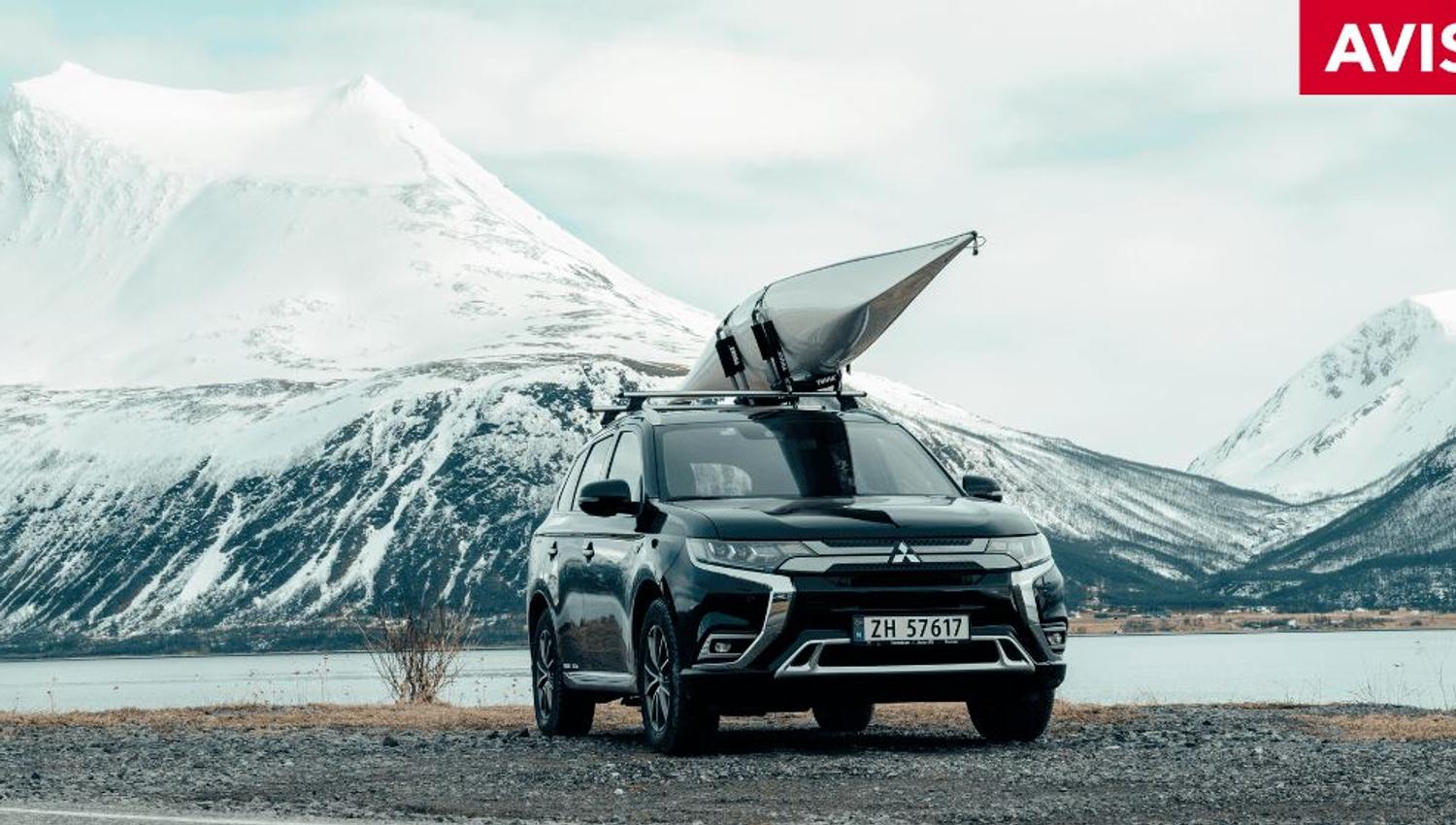Bil med kajakk på taket og fjell i bakgrunnen