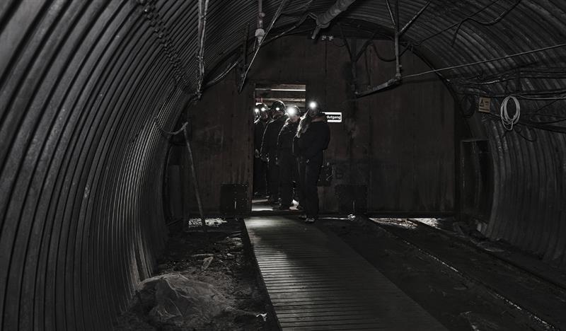 A group of guests with head lamps and helmets on, walking through a mine passage on a guided tour