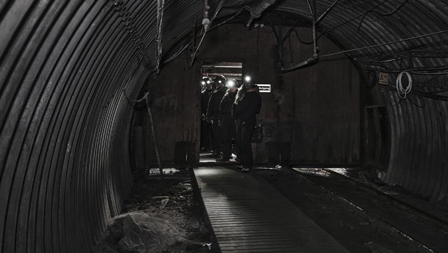 A group of guests with head lamps and helmets on, walking through a mine passage on a guided tour
