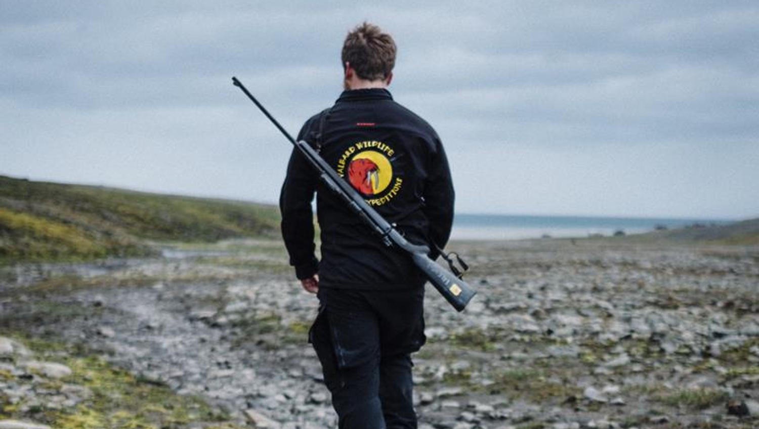 A guide with Svalbard Wildlife Expeditions' logo and a rifle on their back hiking on a trip