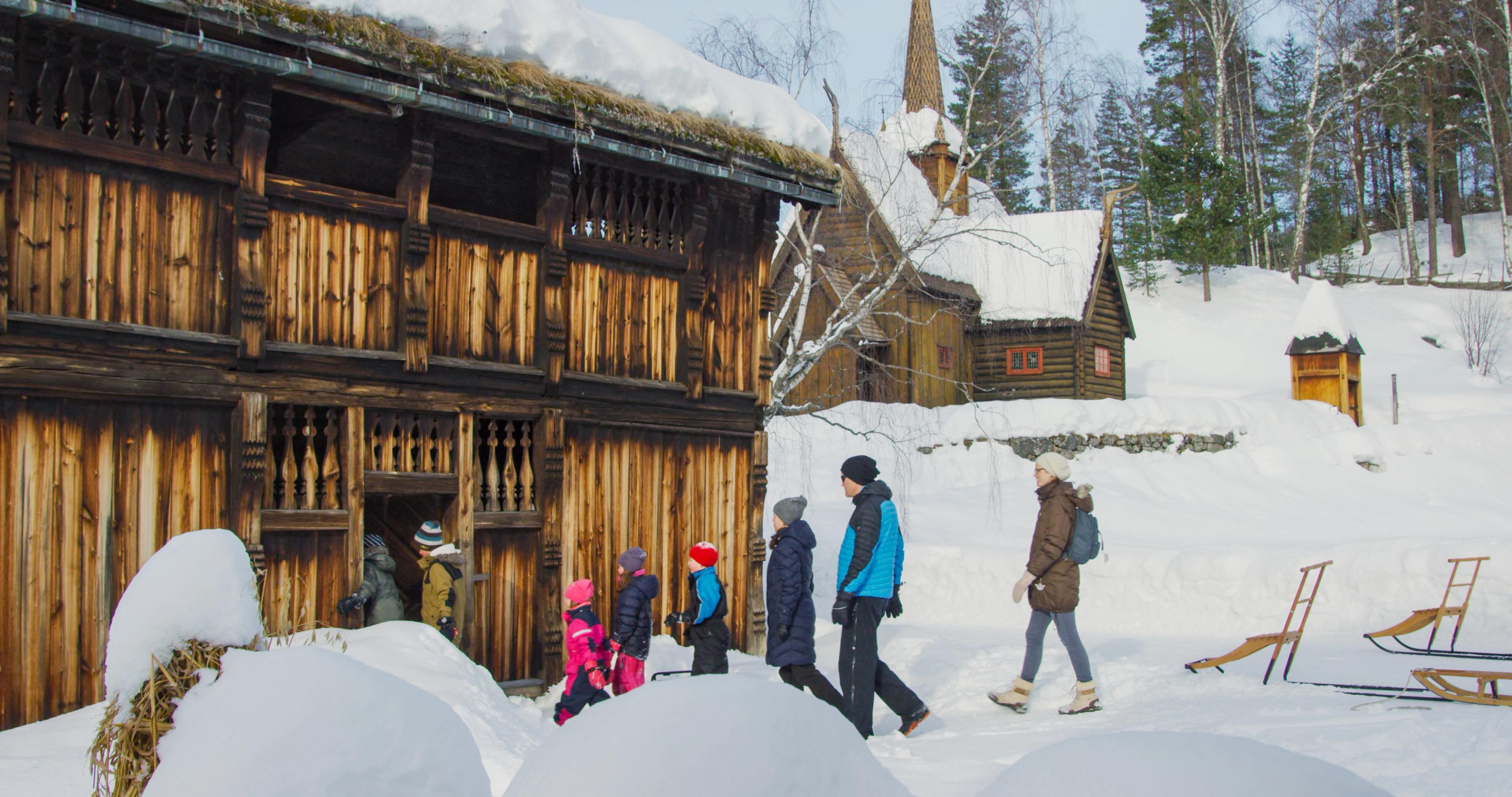 Adults and children entering a historic timber house by Garmo stave church.