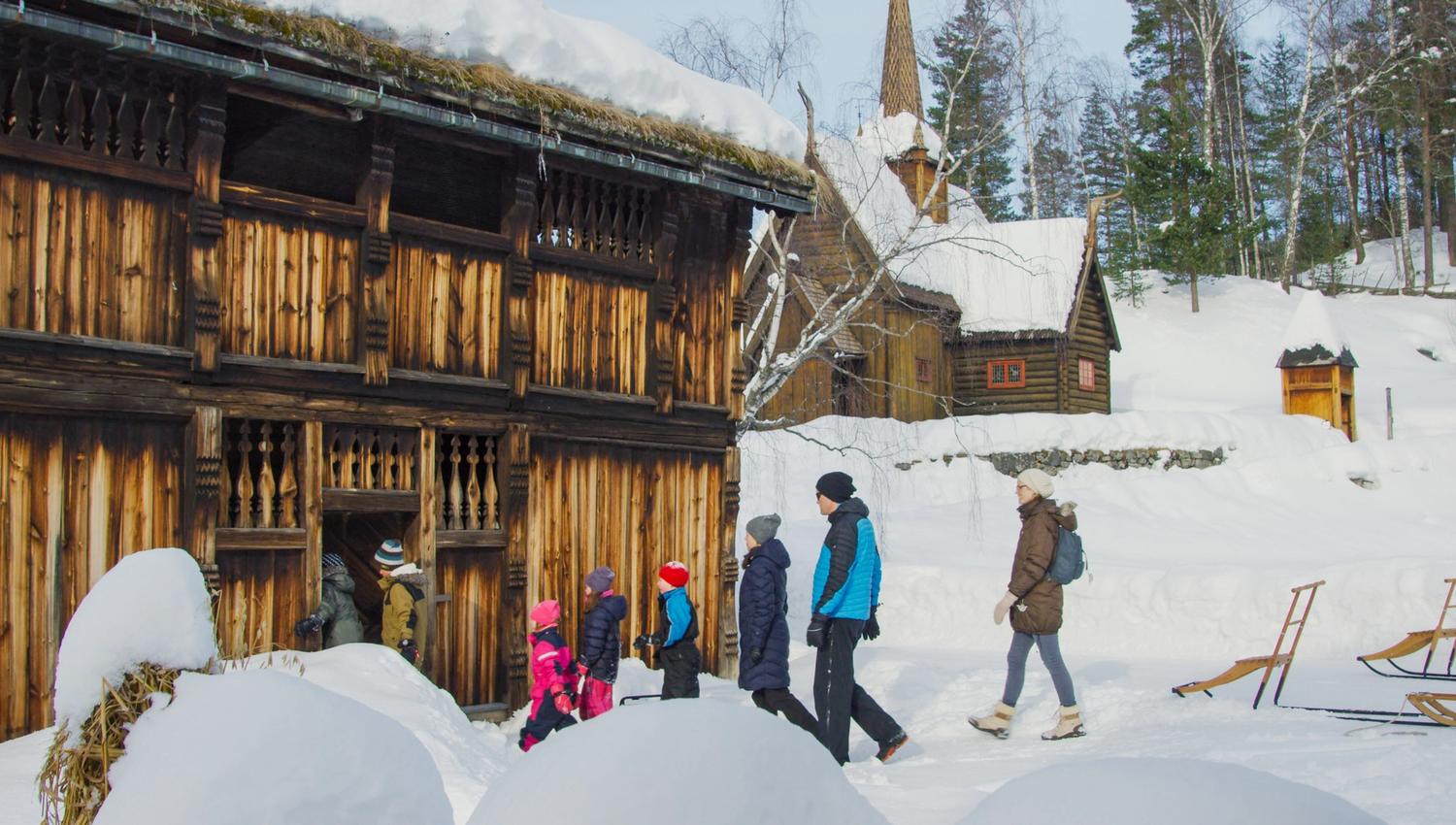 Adults and children entering a historic timber house by Garmo stave church.