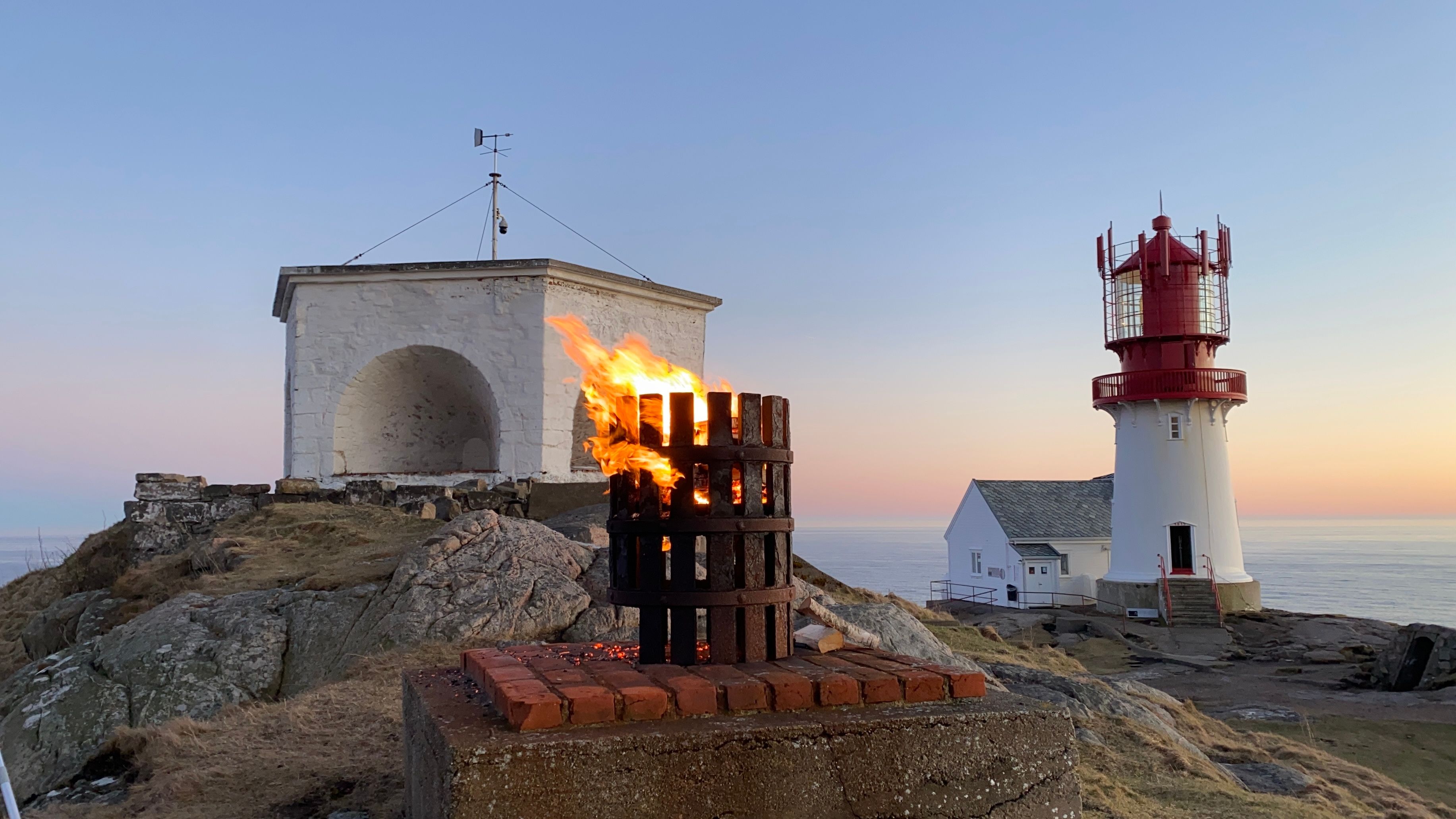 Lindesnes fyr i solnedgang, liten bål midt på bilde