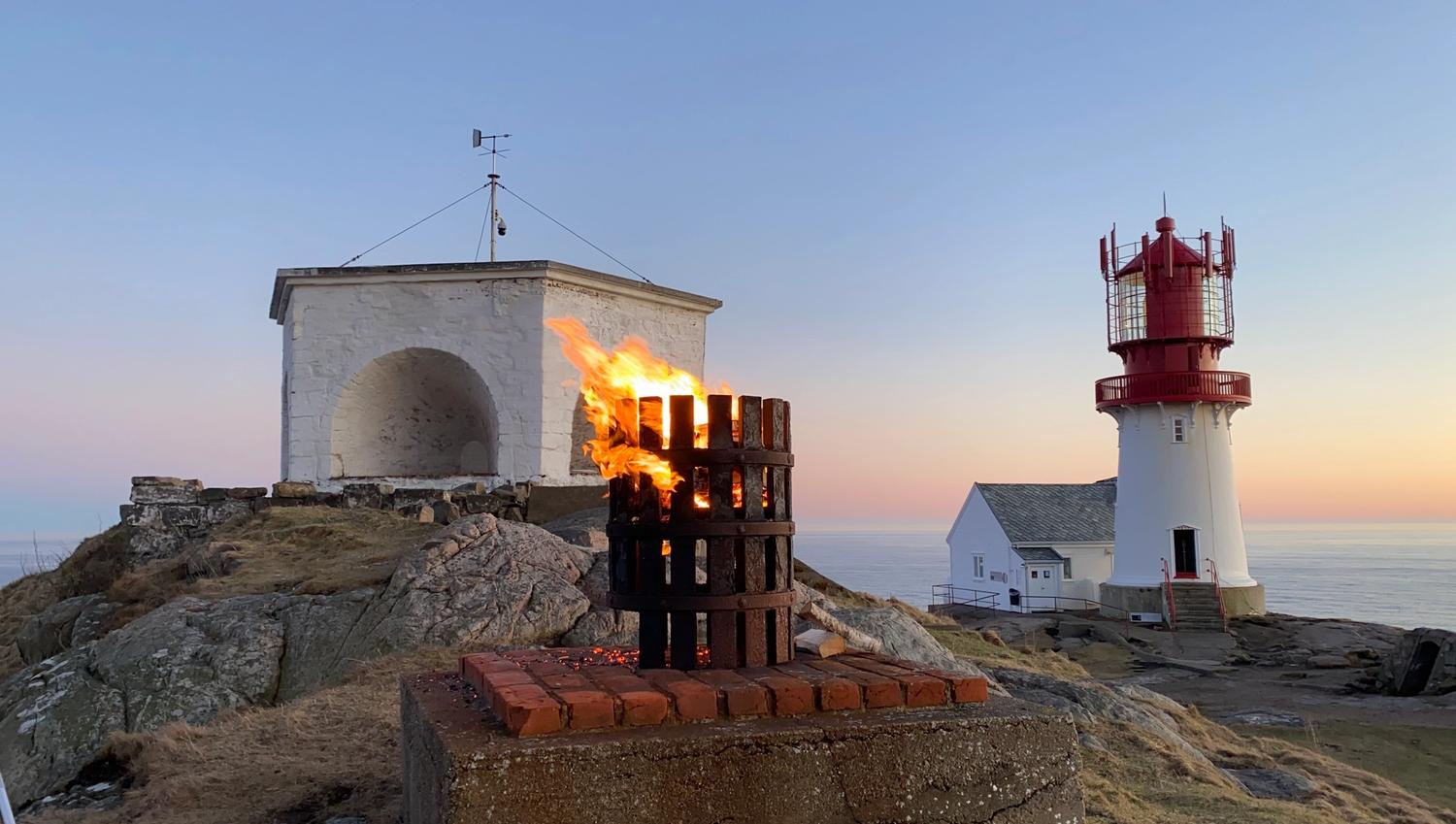 Lindesnes fyr i solnedgang, liten bål midt på bilde