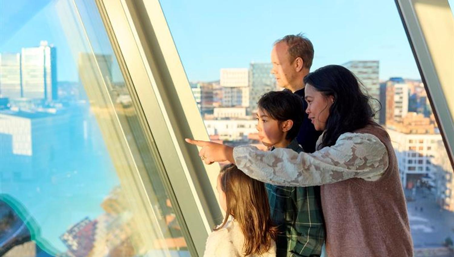 Familie som ser utover byen gjennom et panoramvindu