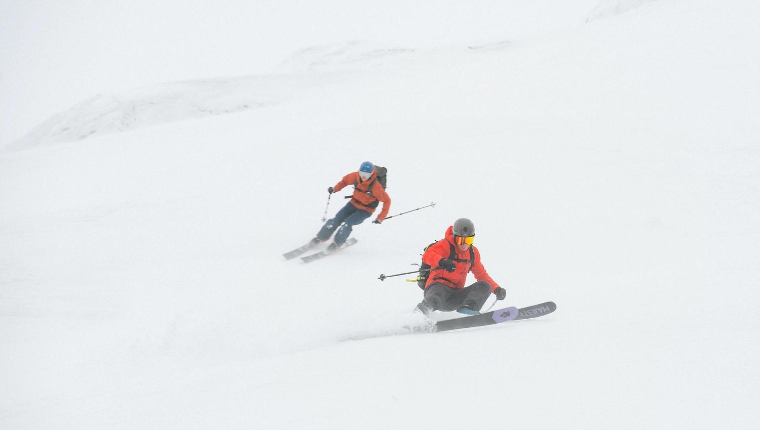 To menn som står på ski i full fart nedover en bakke.