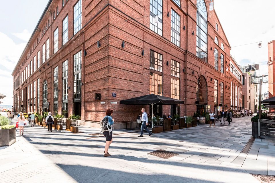 Sidegate med mennesker som går, brun mursteinsbygning, restauranter med uteservering.