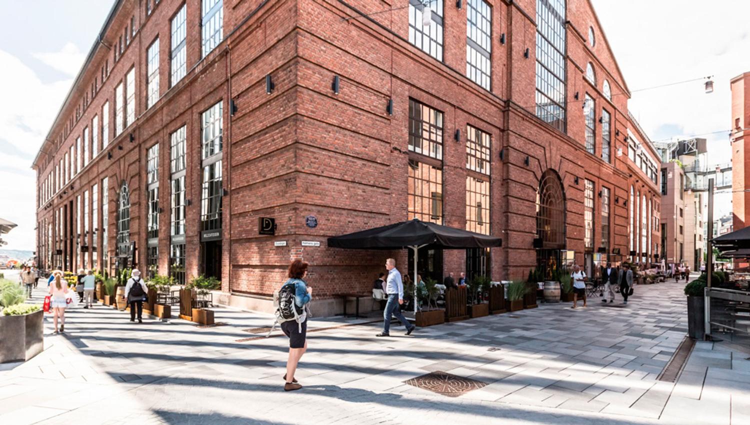 Sidegate med mennesker som går, brun mursteinsbygning, restauranter med uteservering.