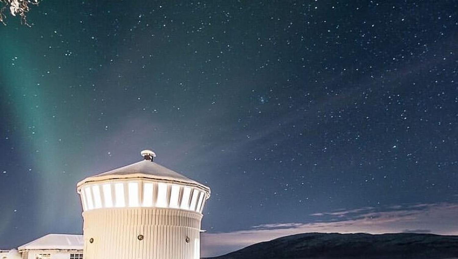 snowy hill, lighthouse with northern lights sky