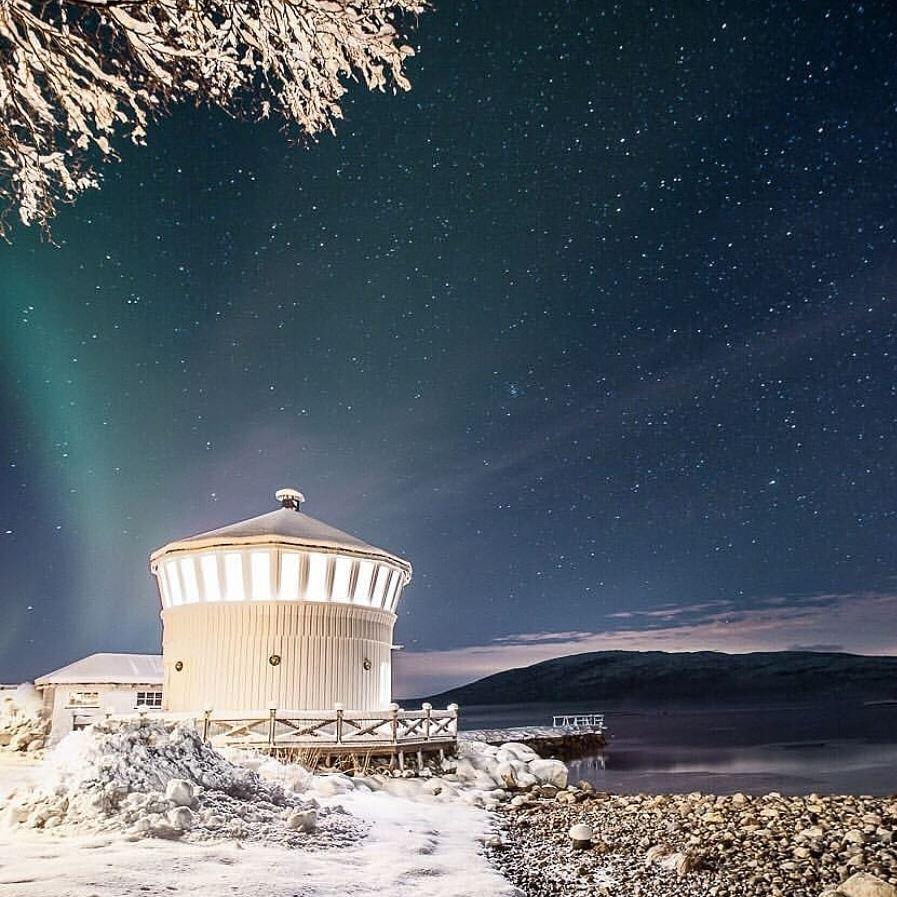 snowy hill, lighthouse with northern lights sky