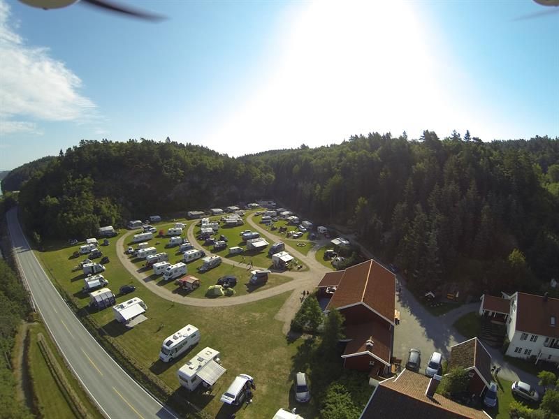 Dronebilde av campingplassen med bobiler/Campingvogner på rekke og rad, med vei i mellom rekkene, hovedvei like ved og skog bak