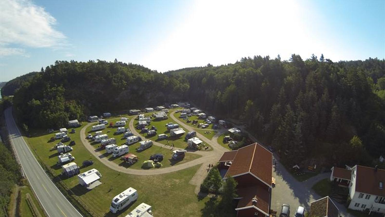 Dronebilde av campingplassen med bobiler/Campingvogner på rekke og rad, med vei i mellom rekkene, hovedvei like ved og skog bak