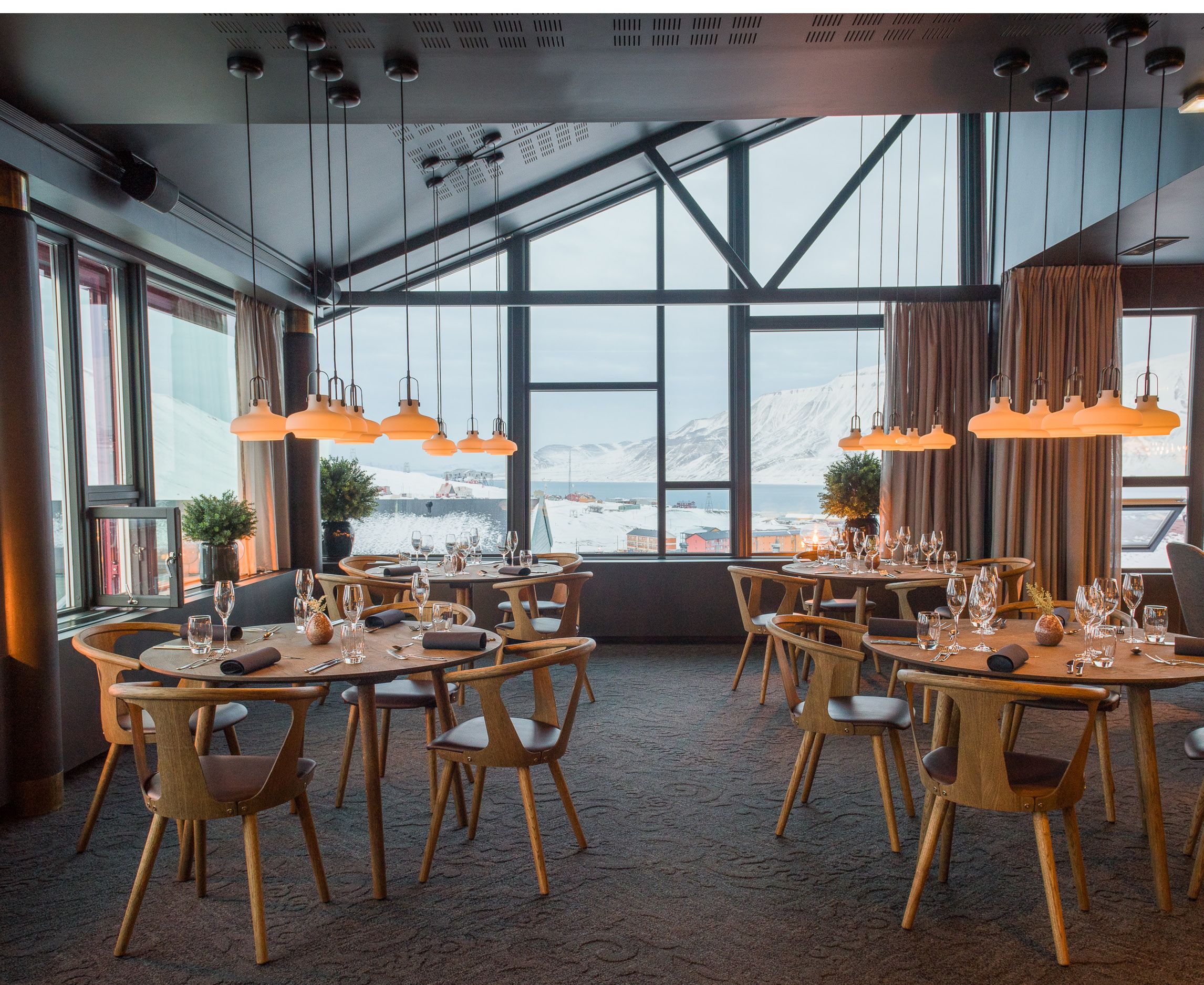 Dekte bord med stoler i en restaurant med utsikt til fjell gjennom vinduer i bakgrunnen