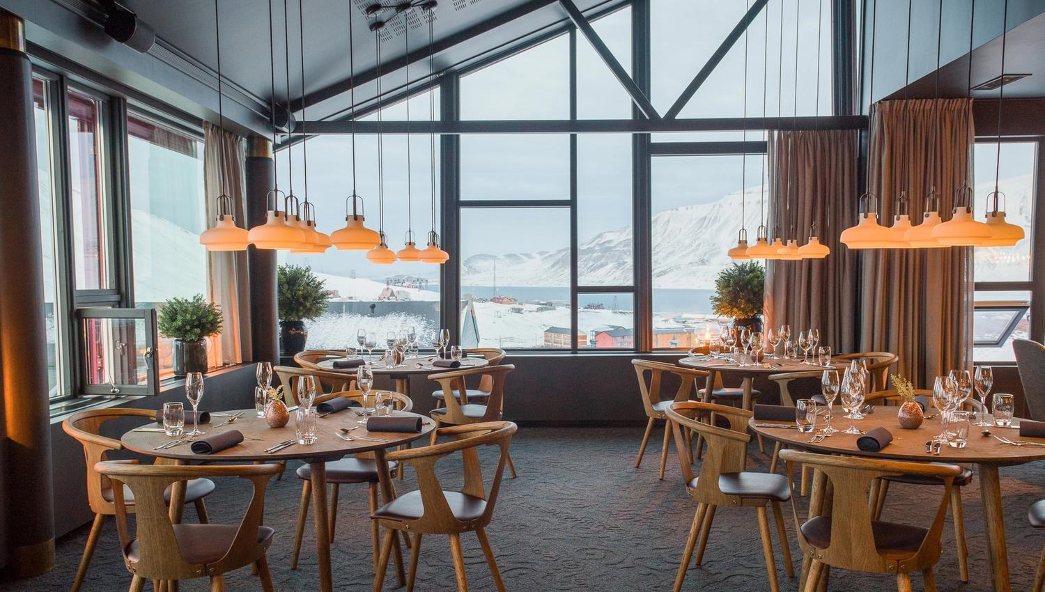 Dekte bord med stoler i en restaurant med utsikt til fjell gjennom vinduer i bakgrunnen