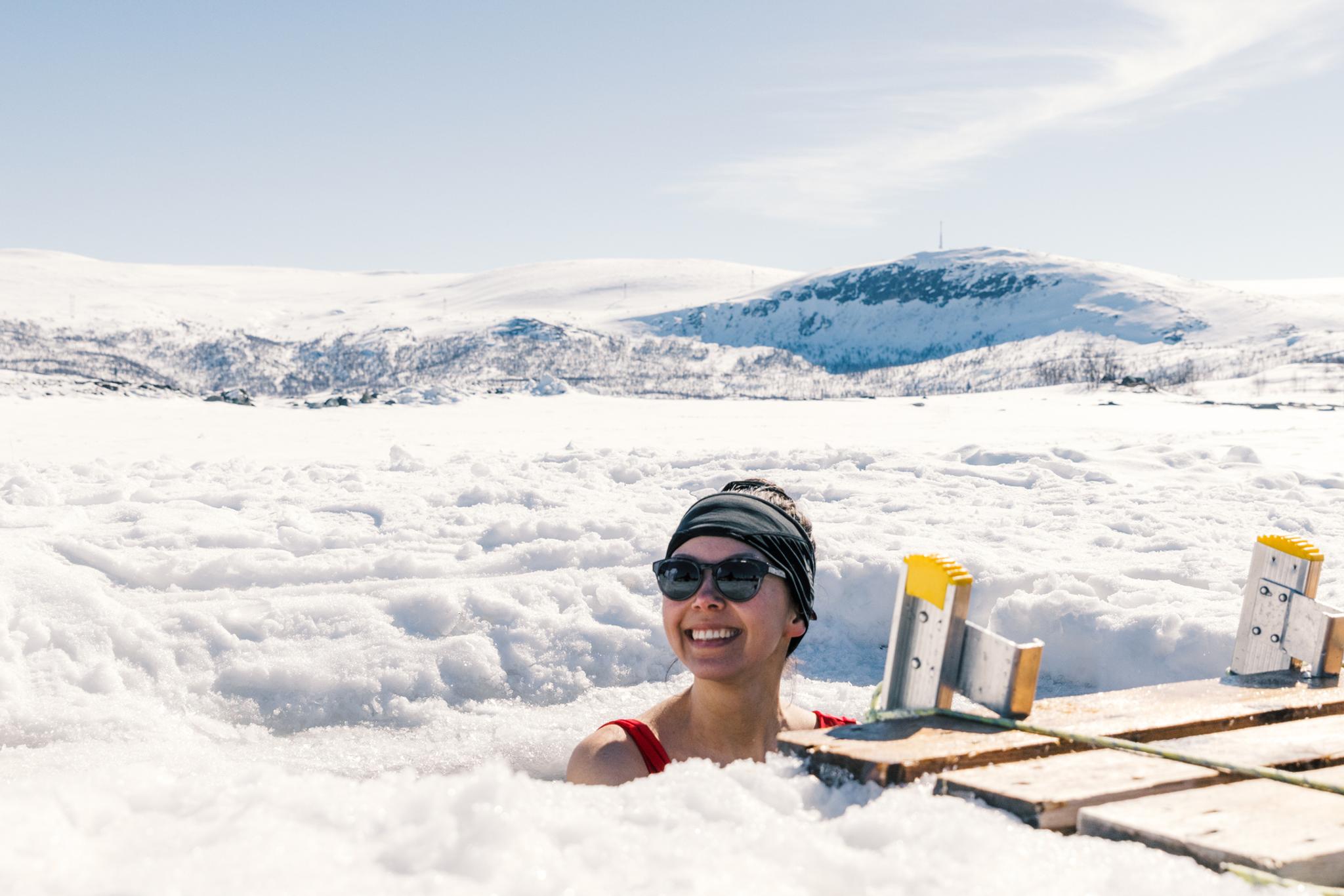 En dame nyter isbading med snølandskapet i bakgrunnen.