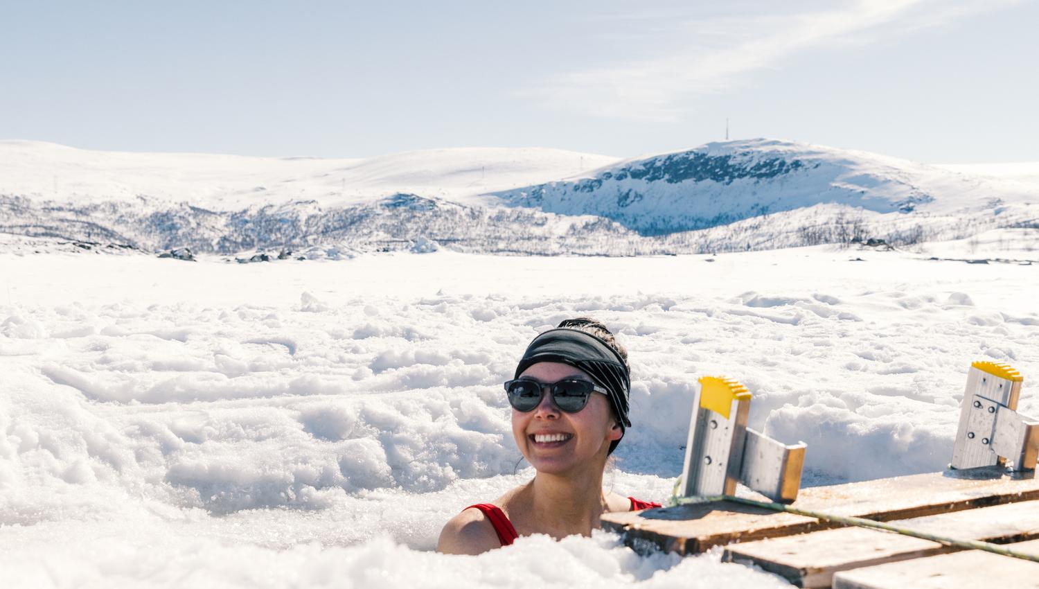 A woman enjoying an ice bath with a snow-covered landscape behind her.