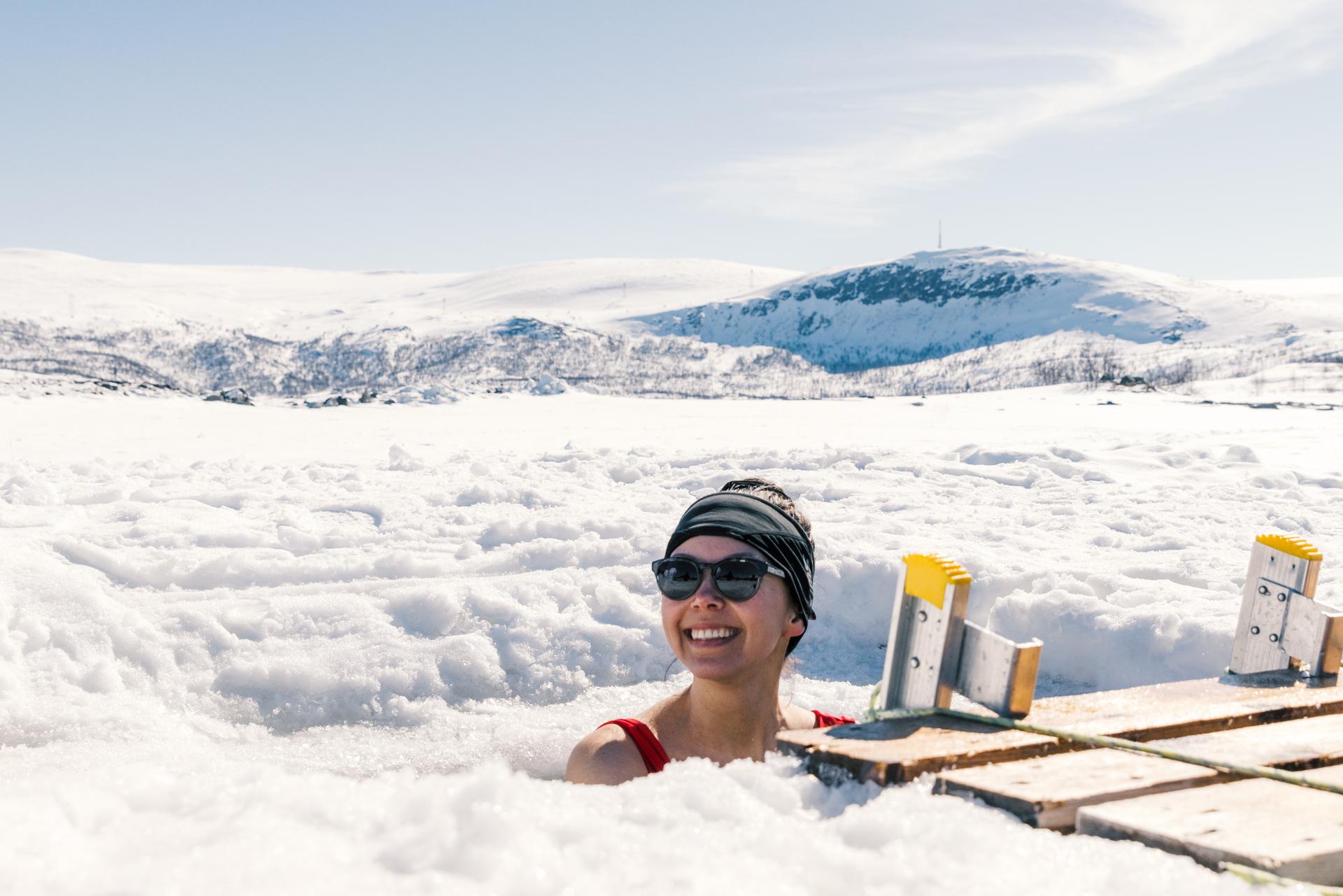 En dame nyter isbading med snølandskapet i bakgrunnen.