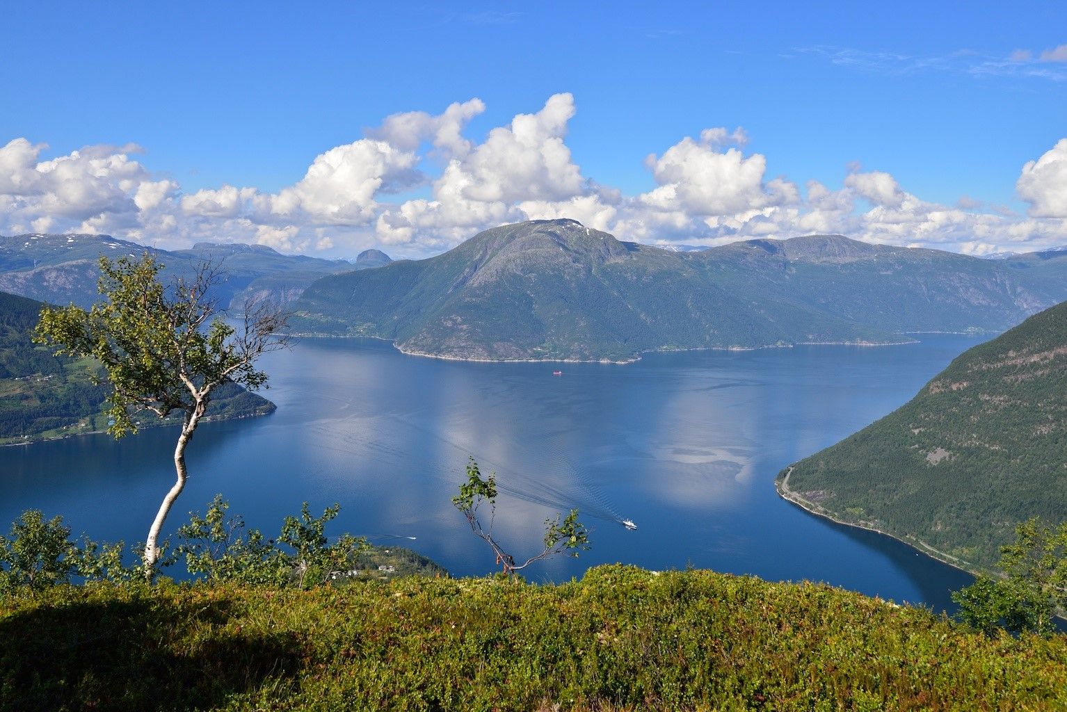 View from Dronningstien over the blue fjord and mountains under a clear sky.