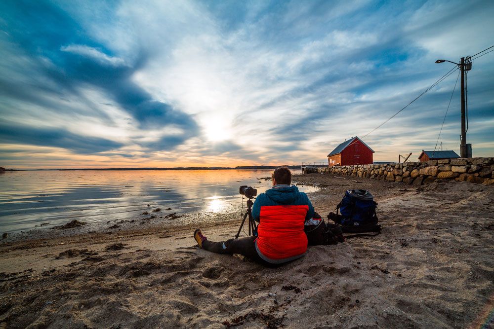 mann sitter på strand på Jomfruland med Kamera