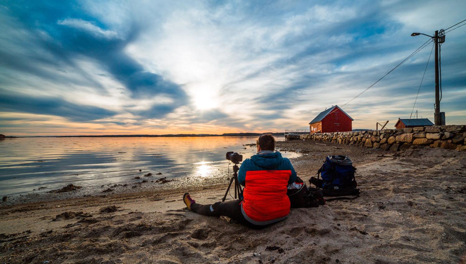 mann sitter på strand på Jomfruland med Kamera