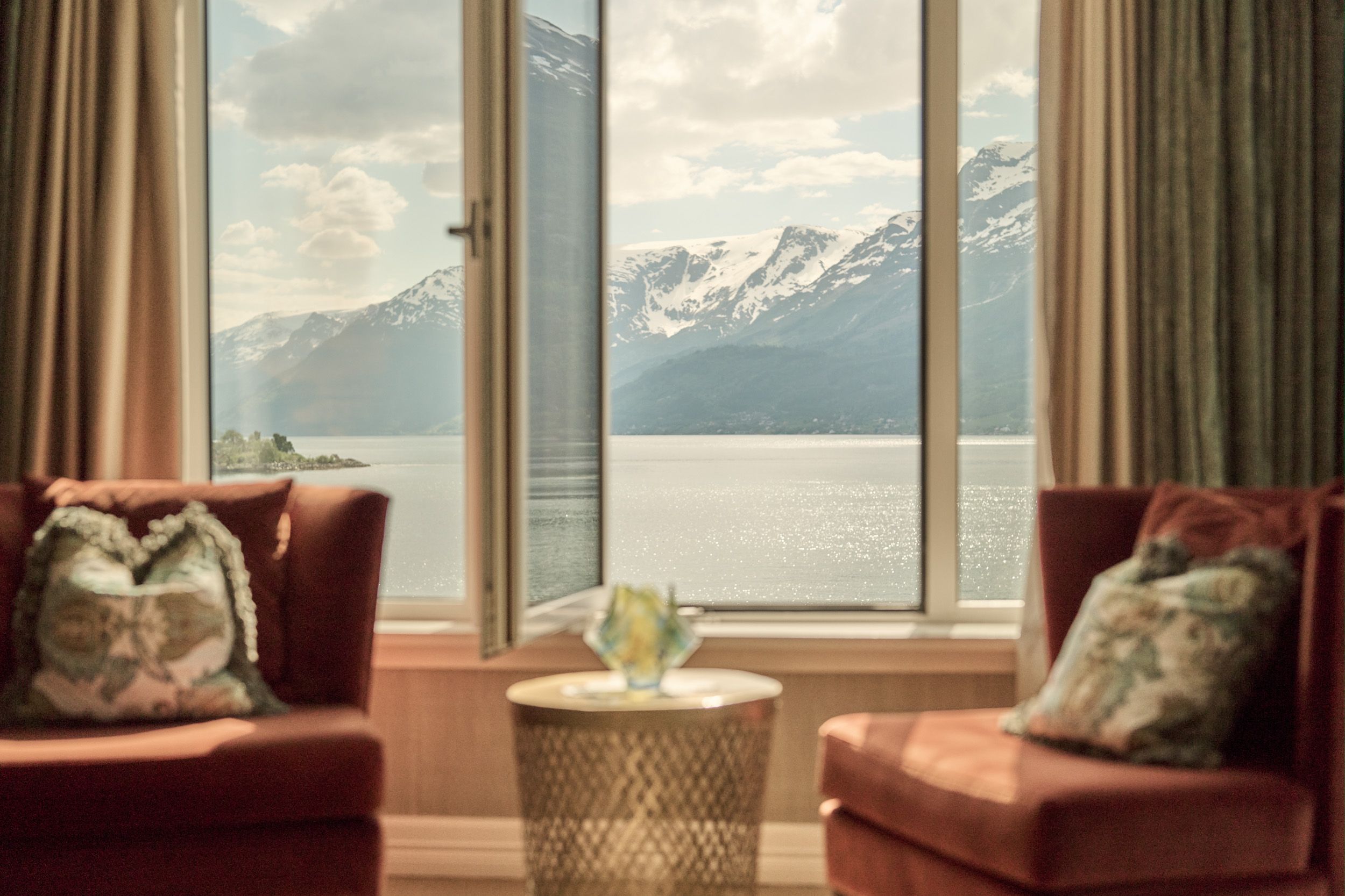 Komfortabel sitjegruppe med opna vindauge og spektakulær fjordutsikt på Hotel Ullensvang.