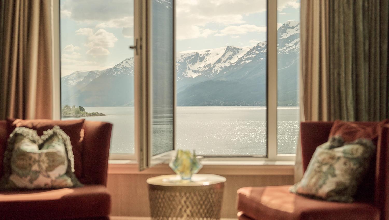 Komfortabel sitjegruppe med opna vindauge og spektakulær fjordutsikt på Hotel Ullensvang.