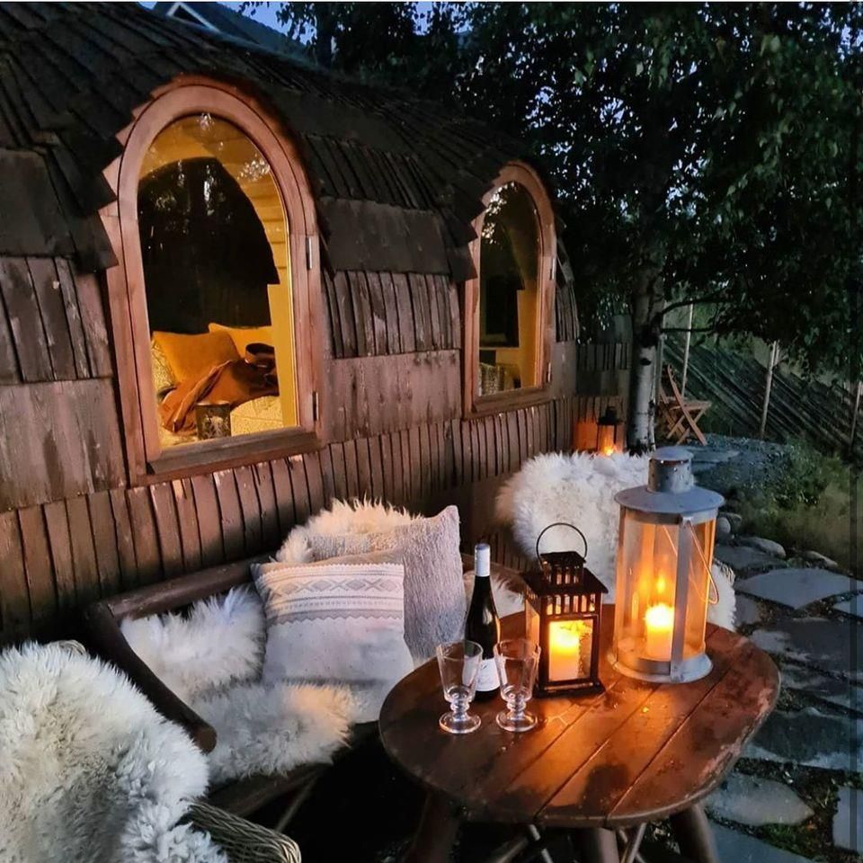 Et stemningsfullt uteområde med trebenker, puter, skinn og tente lanterner.