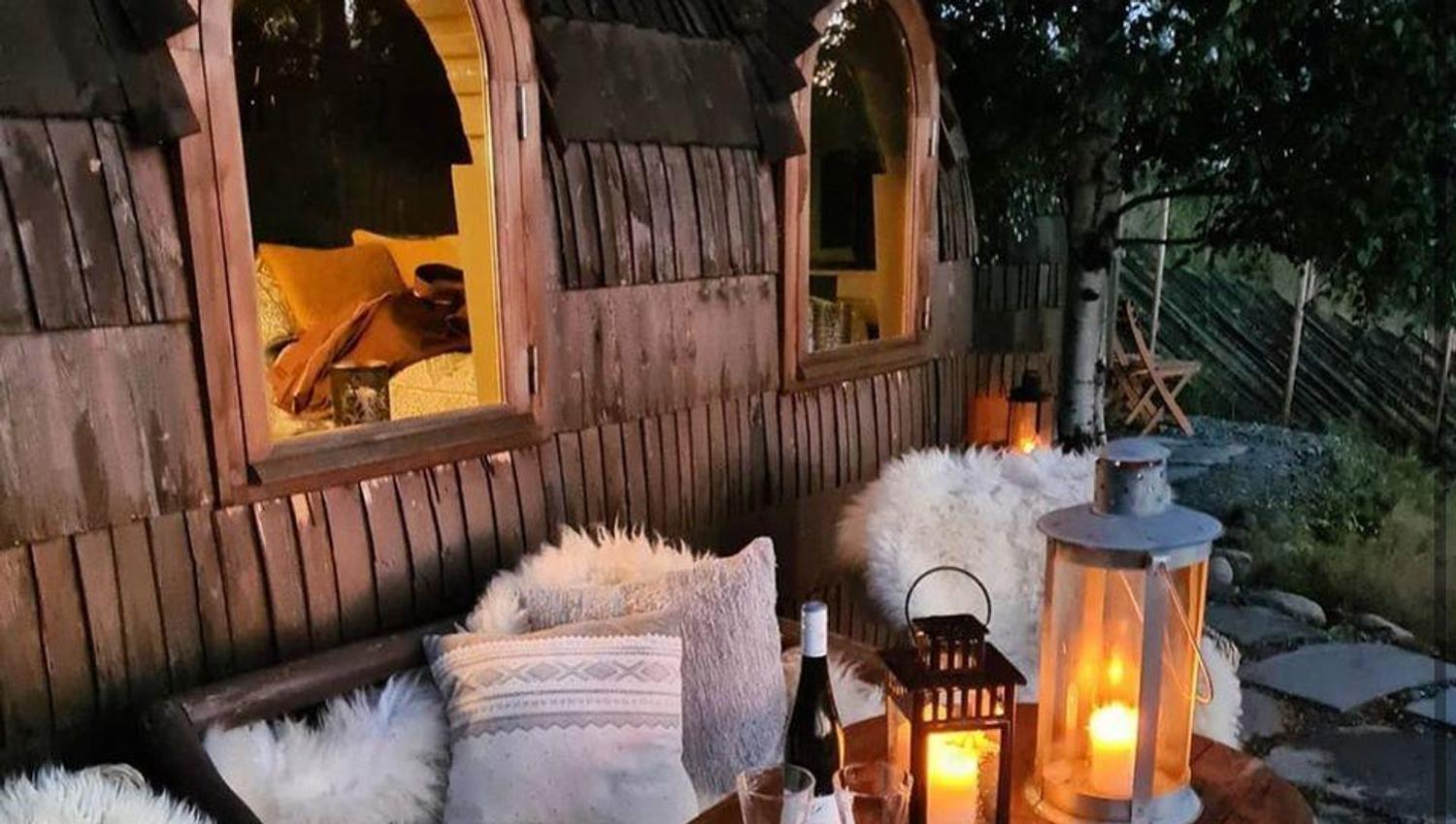 Et stemningsfullt uteområde med trebenker, puter, skinn og tente lanterner.