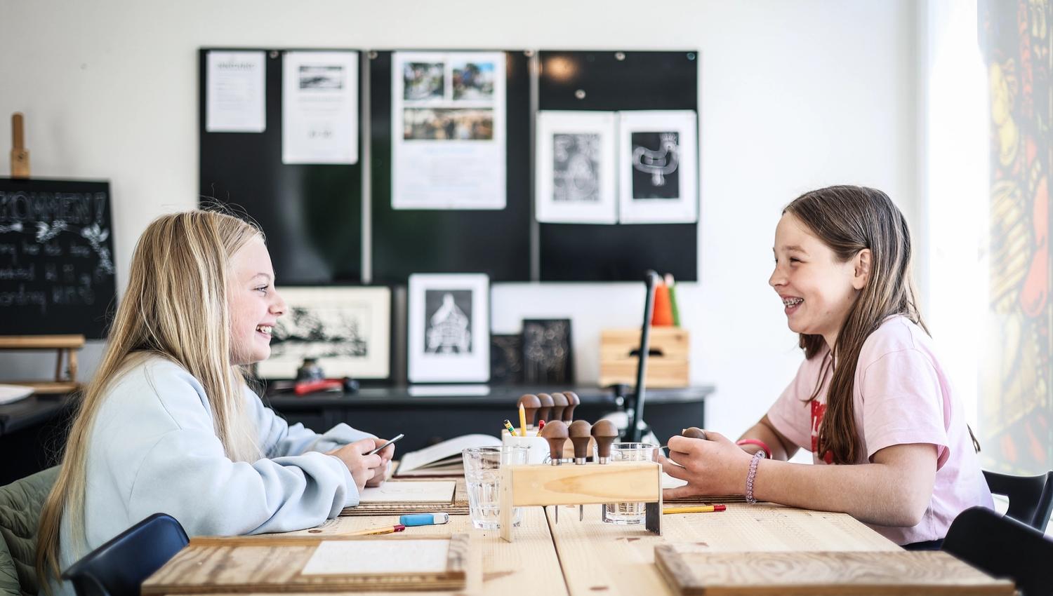 To jenter som smiler stort, som gjør noe håndverk