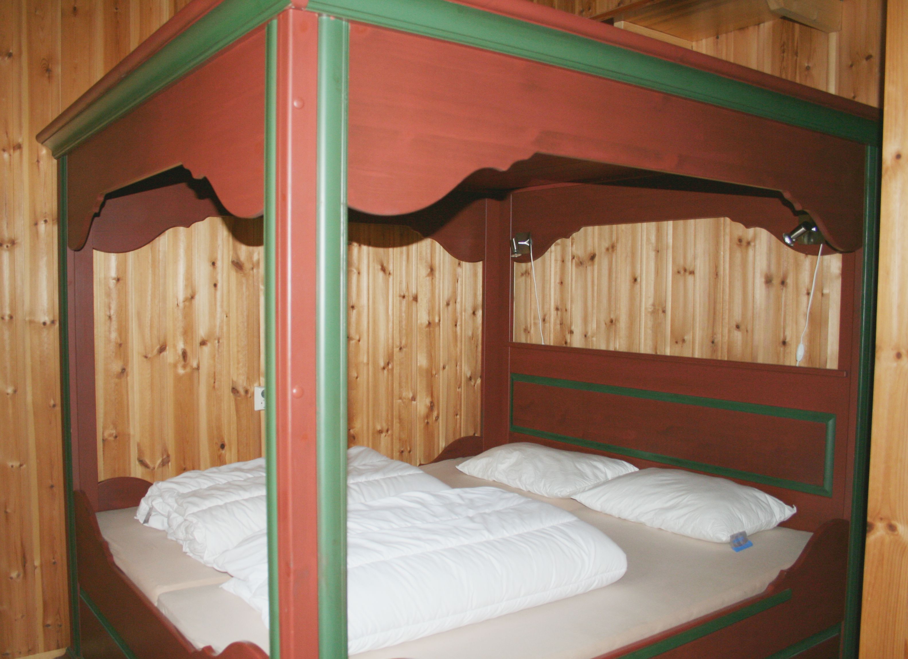 A red wooden four-poster bed, with duvets and pillows in the bed.