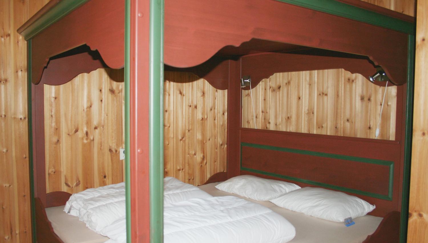 A red wooden four-poster bed, with duvets and pillows in the bed.