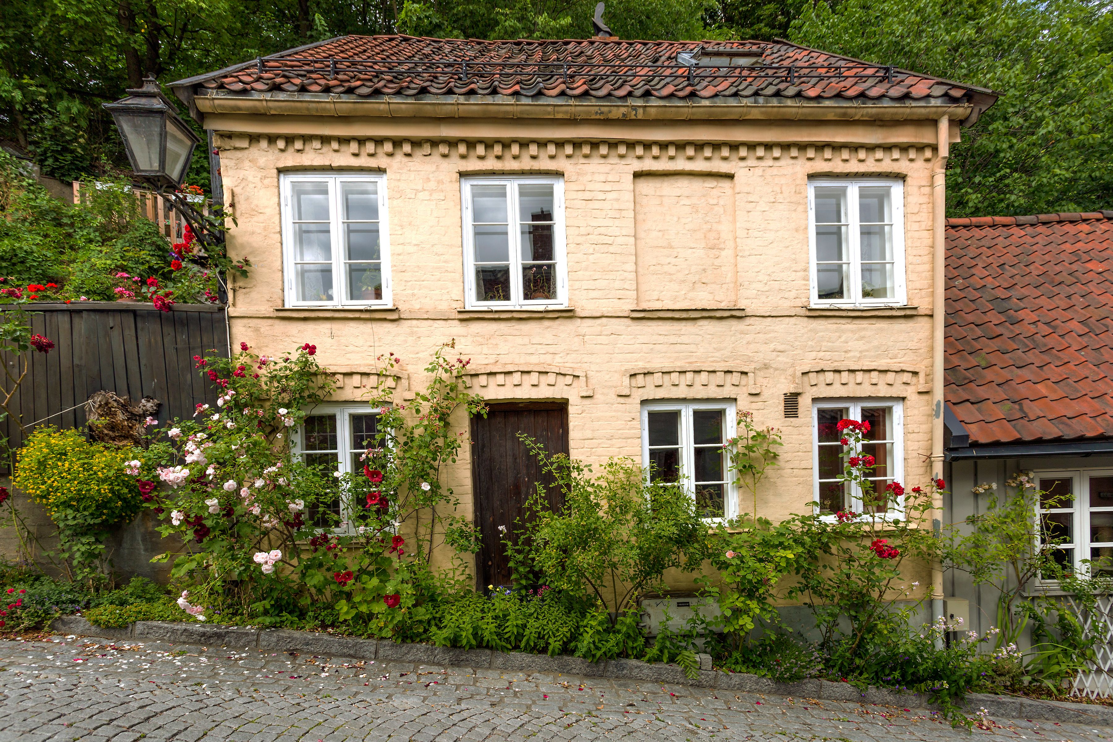 Gammelt murhus med en rekke busker og blomster utenfor.