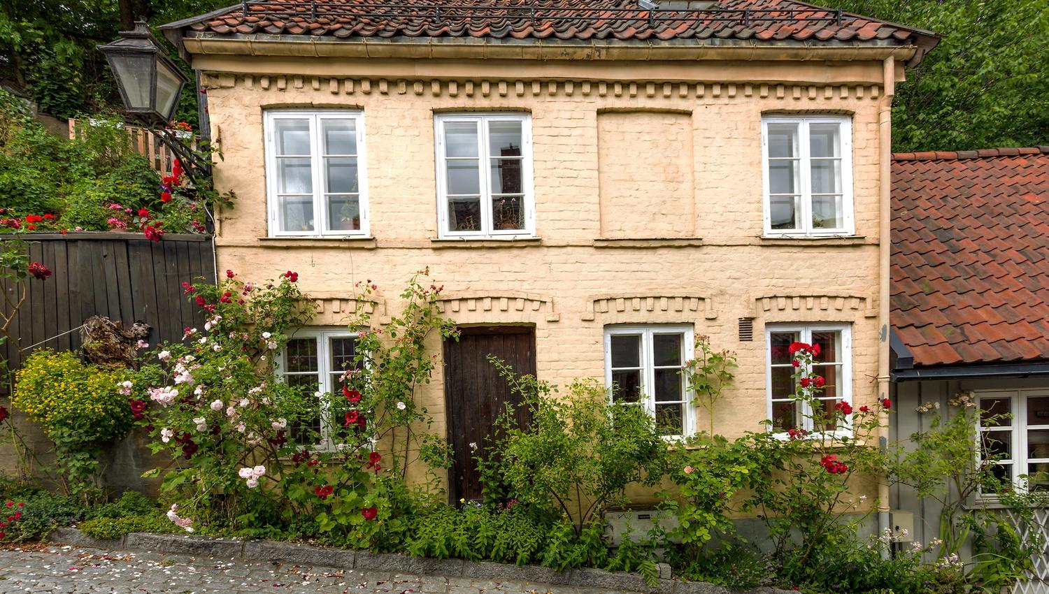 Gammelt murhus med en rekke busker og blomster utenfor.