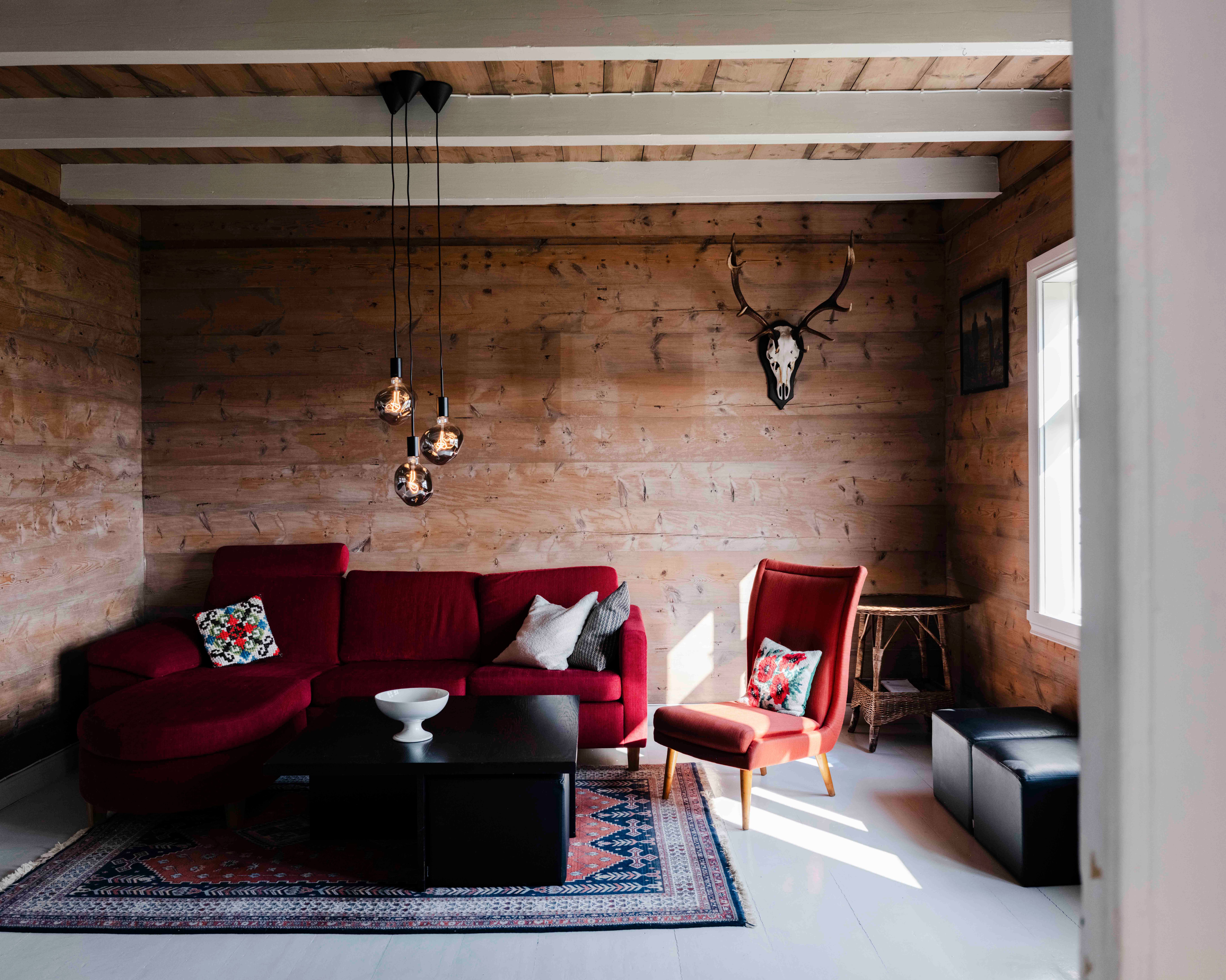 Koselig stove på Stigen Fjordlodge med raud sofa og varm hyttestemning.