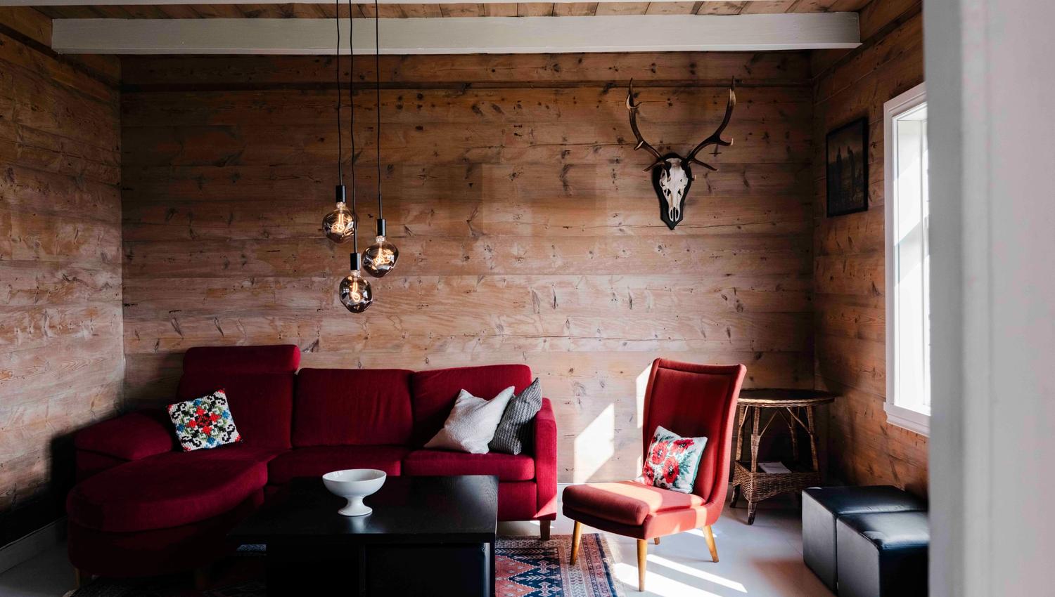 Koselig stove på Stigen Fjordlodge med raud sofa og varm hyttestemning.