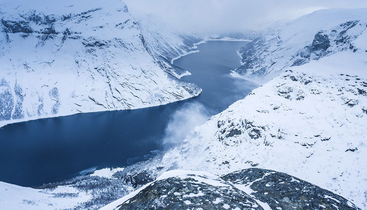 Turgåarar tek ei pause og ser mot solnedgangen over fjella ved Trolltunga.