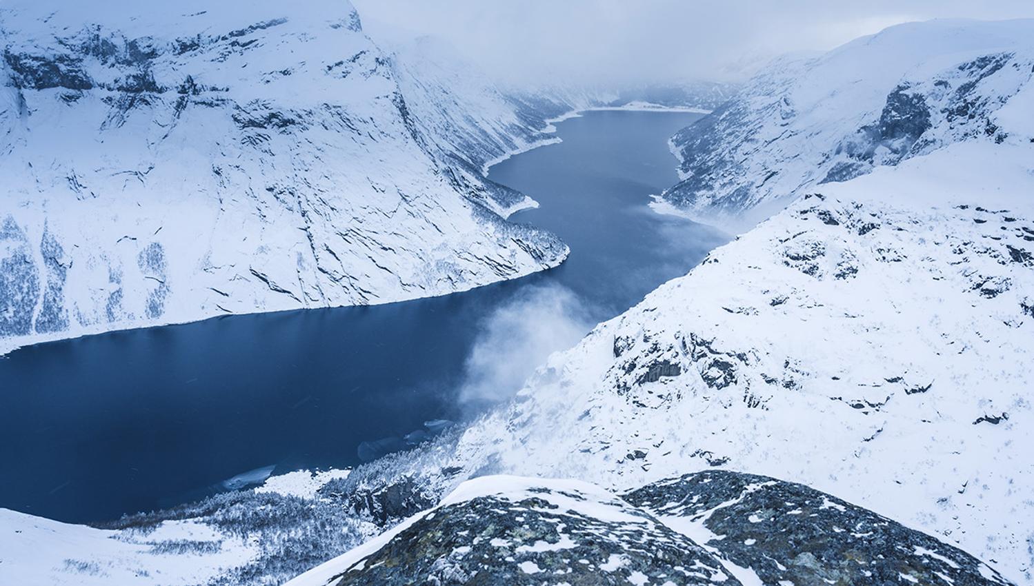Turgåarar tek ei pause og ser mot solnedgangen over fjella ved Trolltunga.