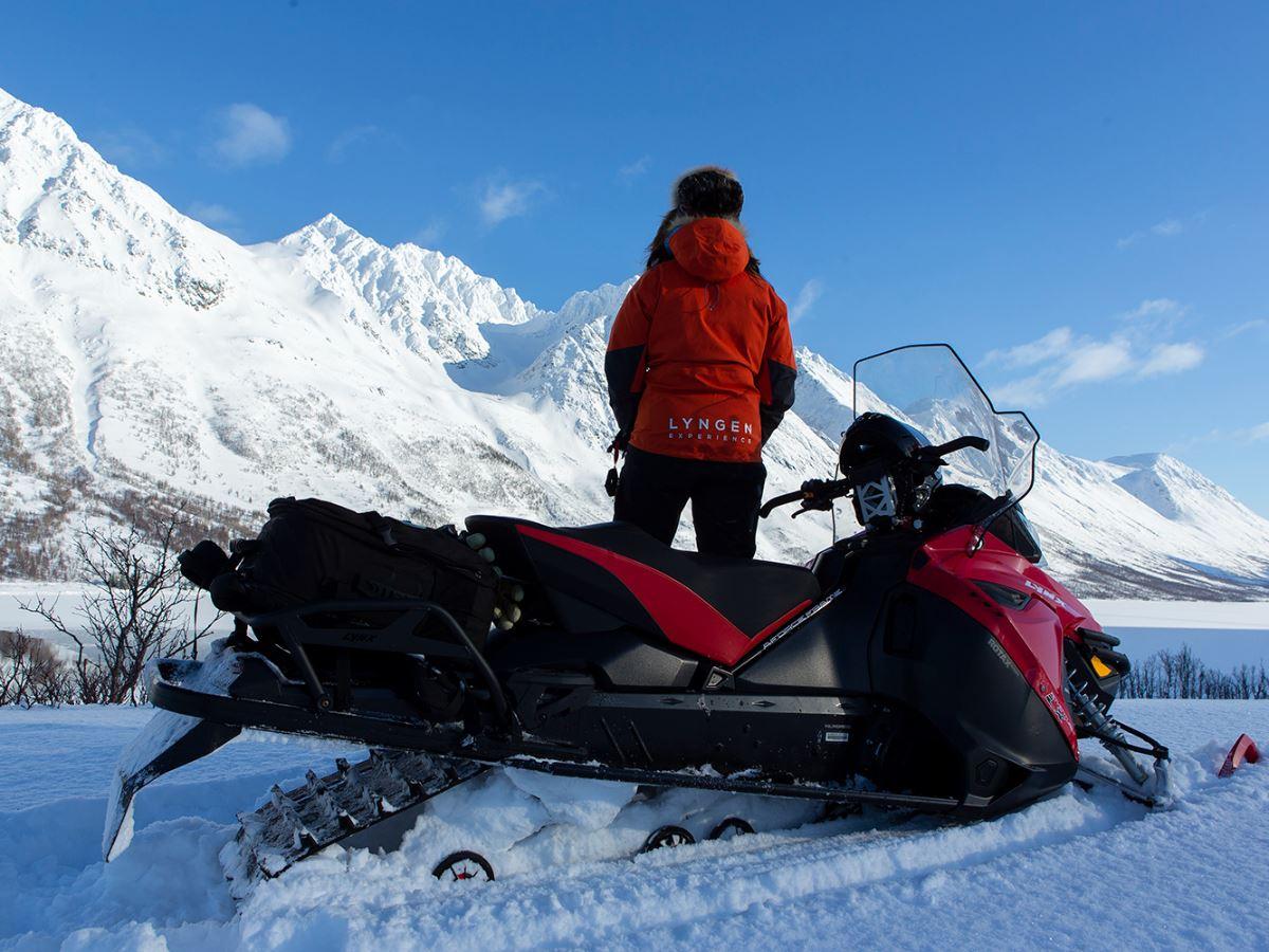 A person standing by a snowmobile and looking at the mountains