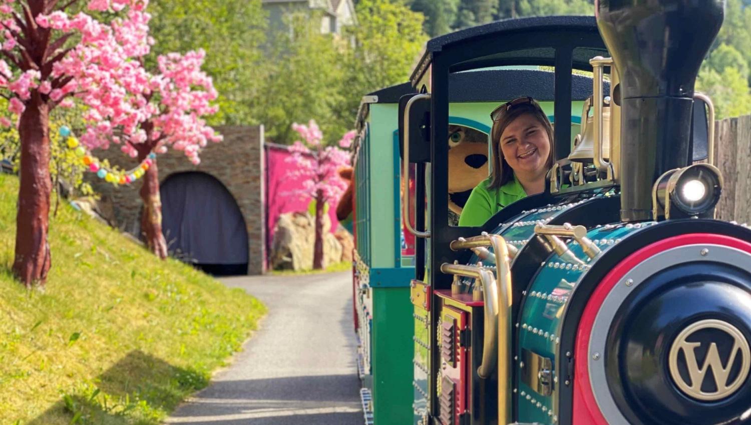 The colourful Mikkel Train with a smiling driver rolls through the blooming Mikkelparken in Kinsarvik.