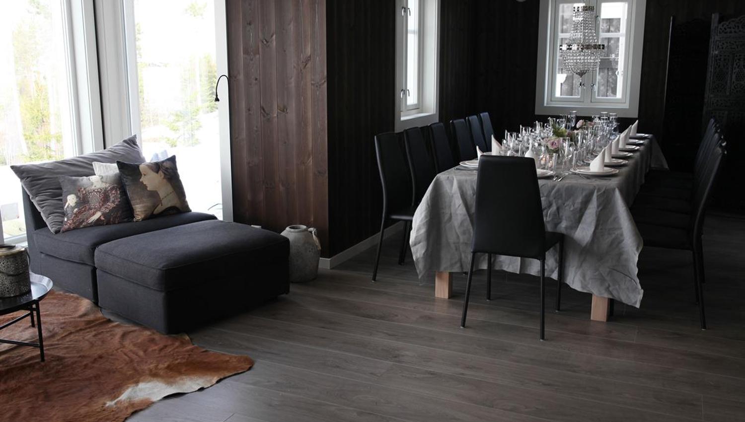 En stue med spisebord og sofa i et rom med mørke trepaneler.