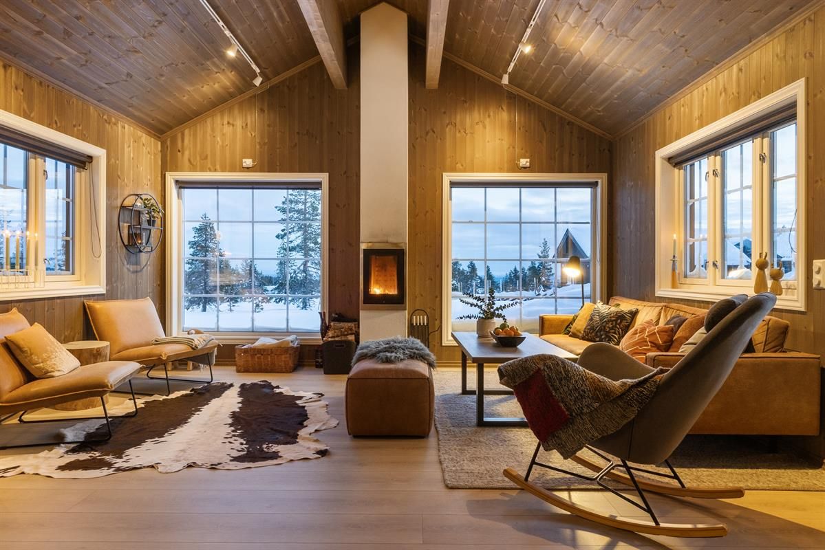 En lys og moderne stue med store vinduer, utsikt mot snødekt natur og en peis.