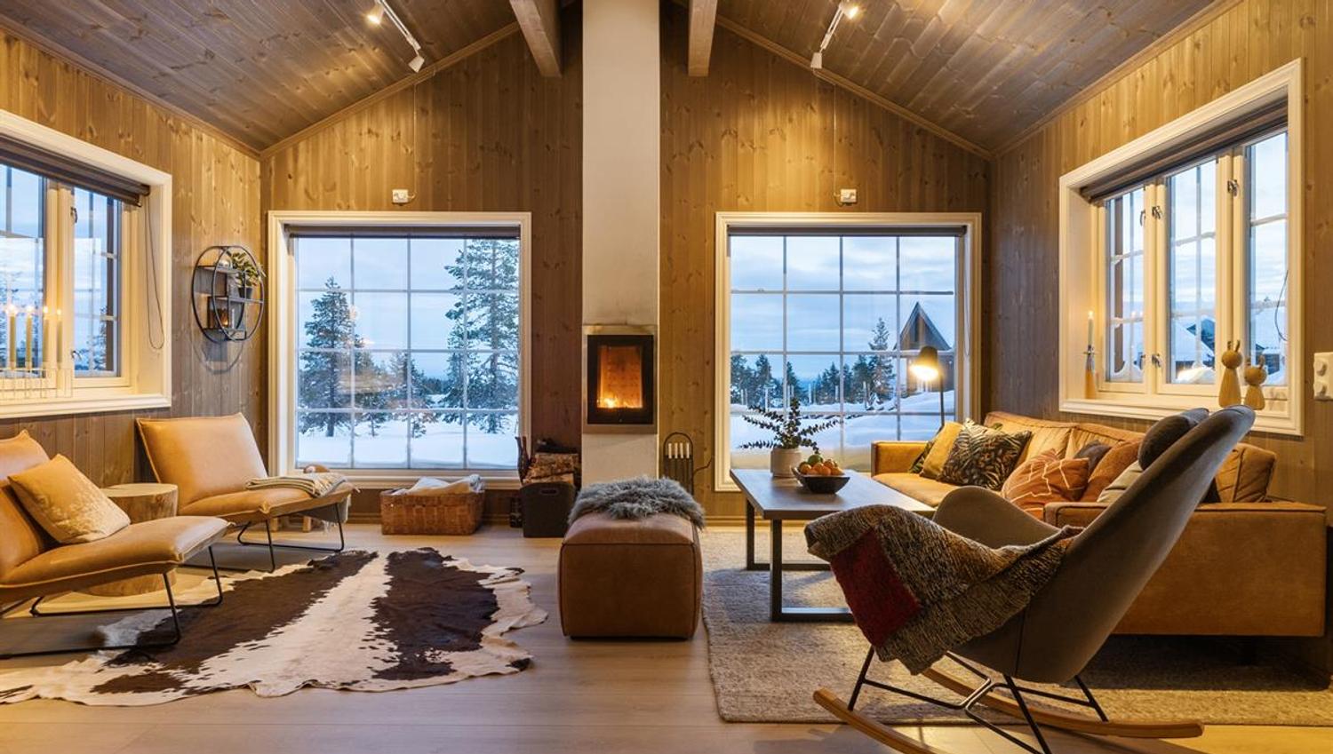 En lys og moderne stue med store vinduer, utsikt mot snødekt natur og en peis.