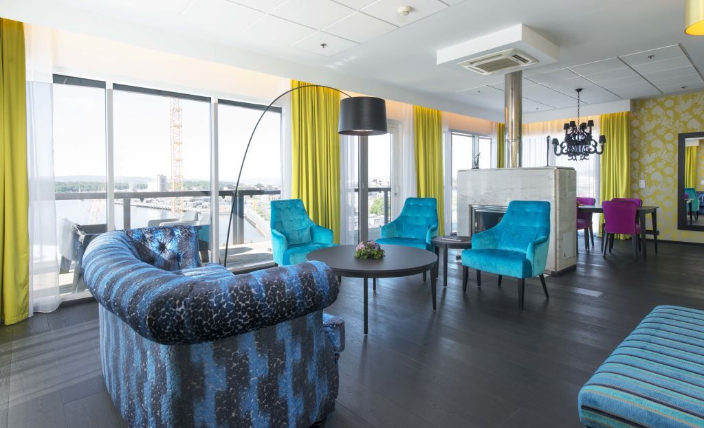 Suite interior with blue armchairs and sofa, coffee table, green curtains and a nice view from the panoramic windows.